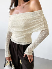 Person wearing a white off-shoulder textured top with black pants against a plain background