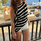 Striped asymmetrical knit top worn by a model on a balcony overlooking the sea.