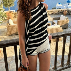 Striped asymmetrical knit top worn by a model on a balcony overlooking the sea.