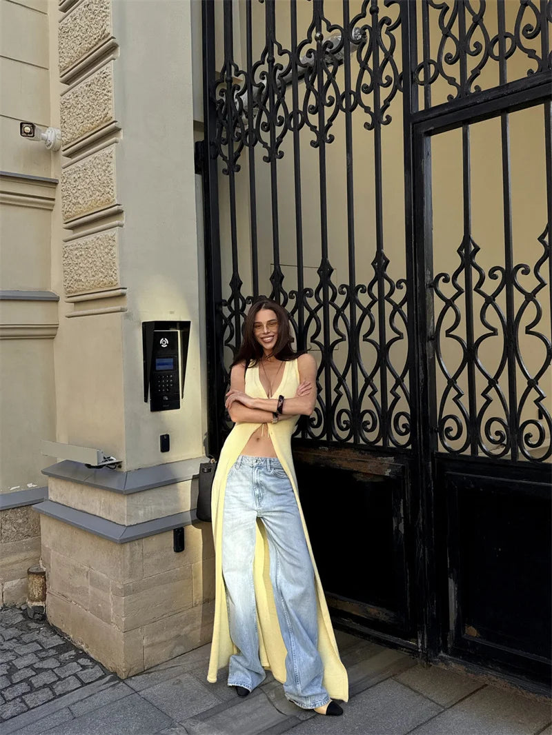Woman in a yellow dress and blue jeans standing next to a building entrance with decorative black metal gate.