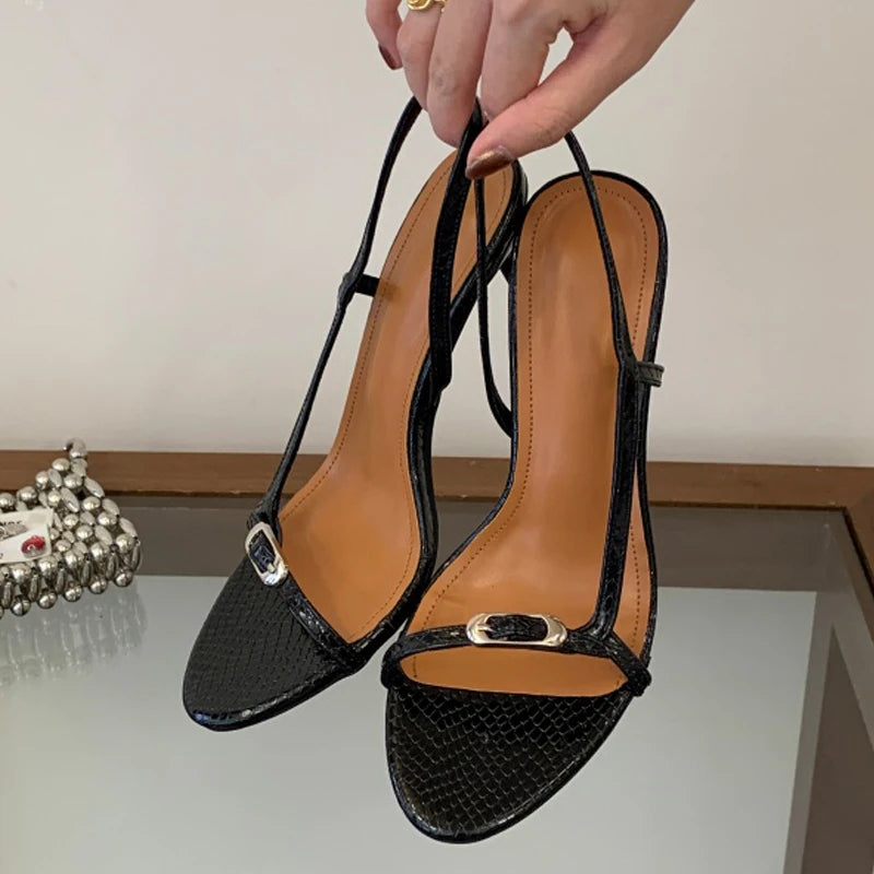 Hand holding black thin strap buckle stiletto heels