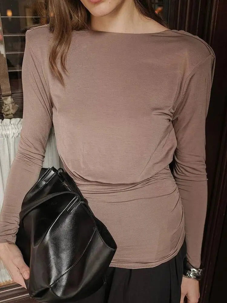 Person wearing a brown long-sleeve top holding a black clutch.