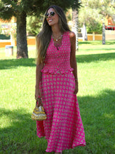 Woman in a pink patterned dress standing in a grassy area with trees in the background