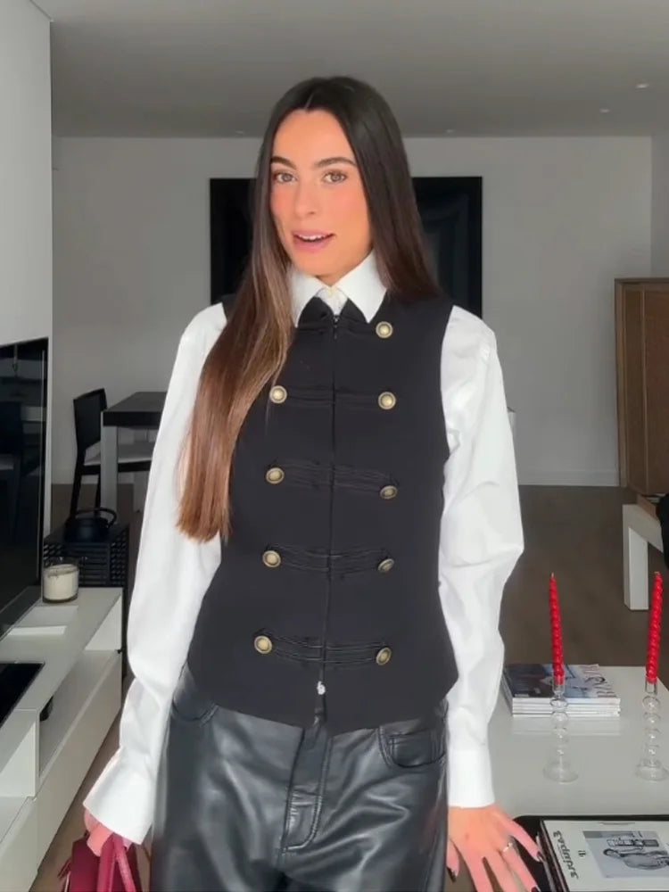 Person wearing a black vest with gold buttons over a white shirt in a kitchen.