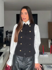 Person wearing a black vest with gold buttons over a white shirt in a kitchen.
