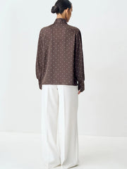 Person wearing a brown polka dot blouse and white pants on a white background