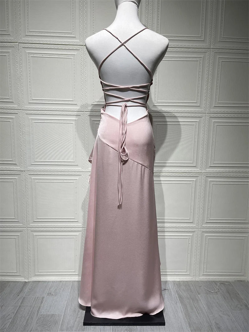 Pink evening gown with criss-cross straps on a mannequin against a gray paneled wall.