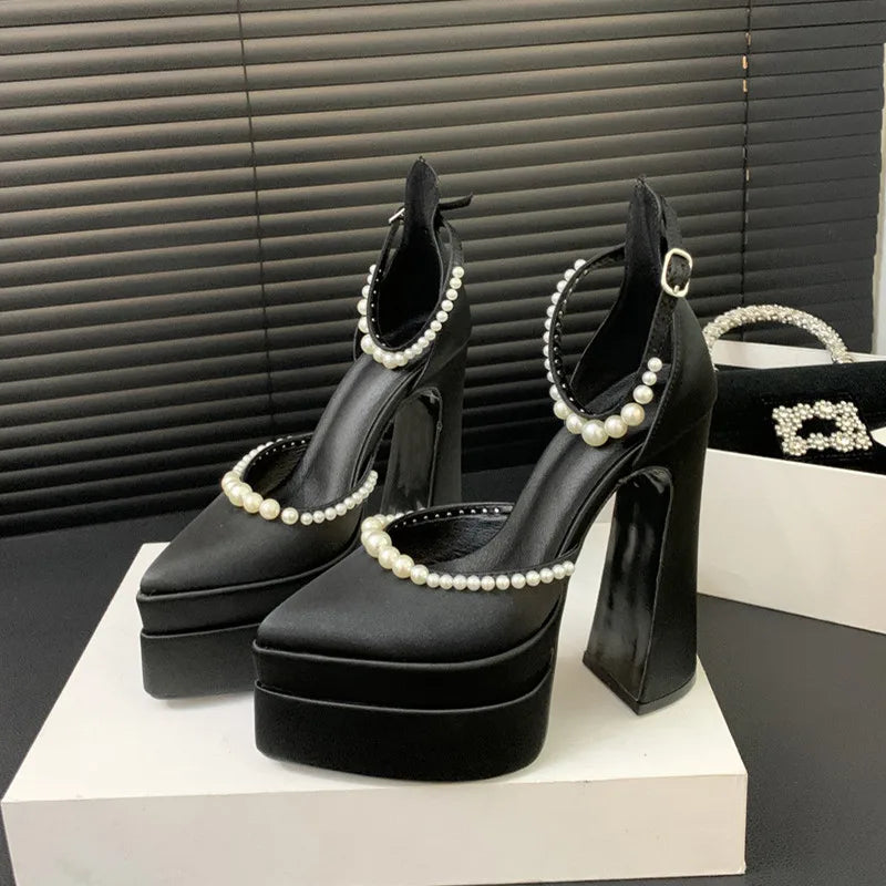 Black high-heeled shoes with pearl embellishments on a white platform against a black background.
