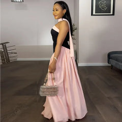 Woman in a black and pink dress holding a handbag in a room with a couch and plant.