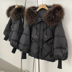 Black puffer jacket with fur hood on a hanger against a white wall.