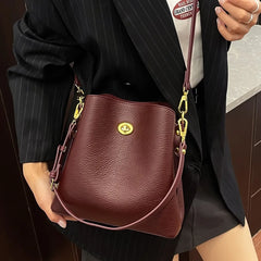 Person holding a brown leather handbag with a gold clasp.