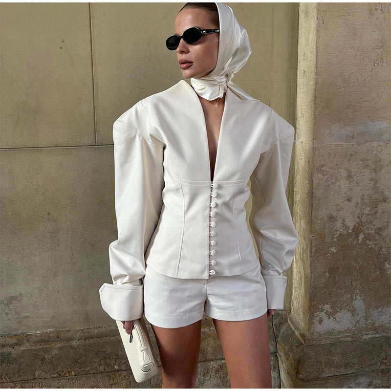Woman in a white outfit with a headscarf standing against a textured wall.