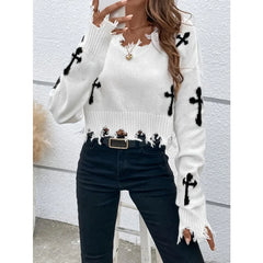 White sweater with black cross patterns worn by a person against a white wall.