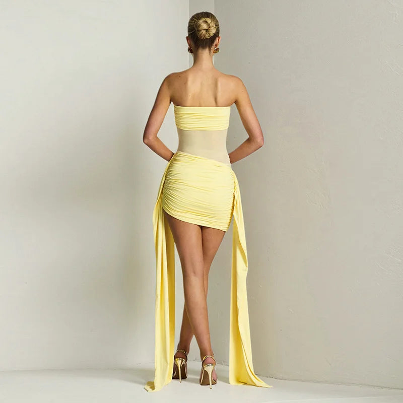 Woman wearing a yellow strapless dress with a high slit on a plain background
