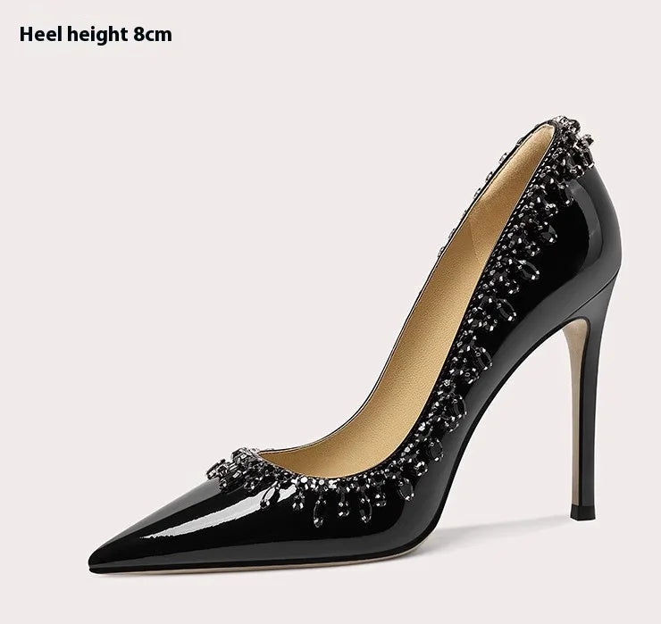 Black high-heeled shoe with decorative elements on a light gray background