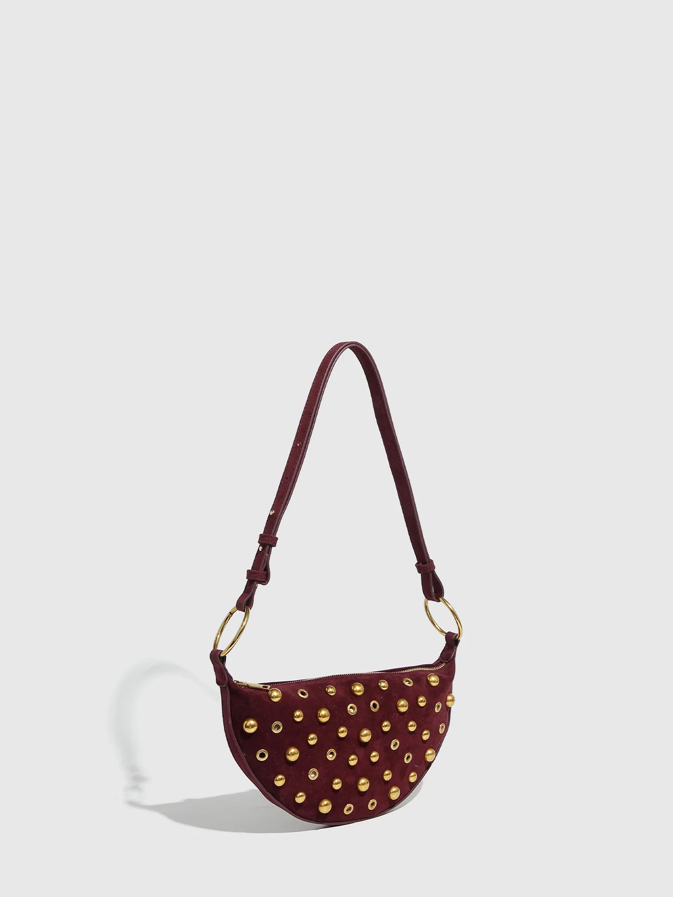 Brown handbag with gold studs and a strap on a light gray background