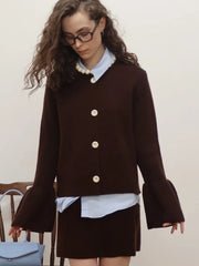 Woman wearing a brown bell-sleeve jacket with gold buttons on a plain background