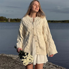 Woman in a cream cable knit cardigan by a lake holding flowers.