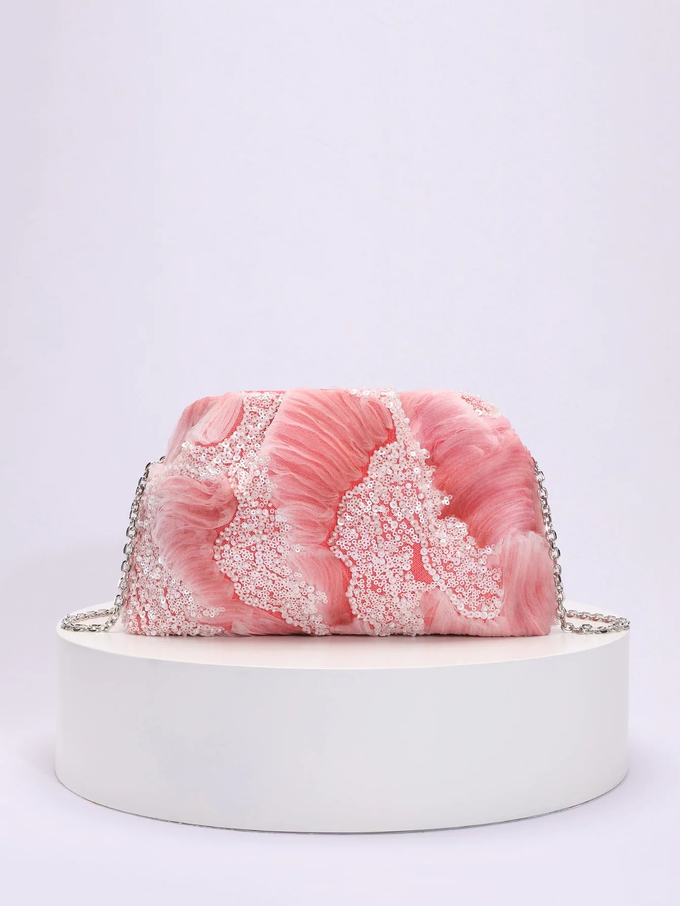 Pink textured handbag with a chain strap on a white platform against a light gray background