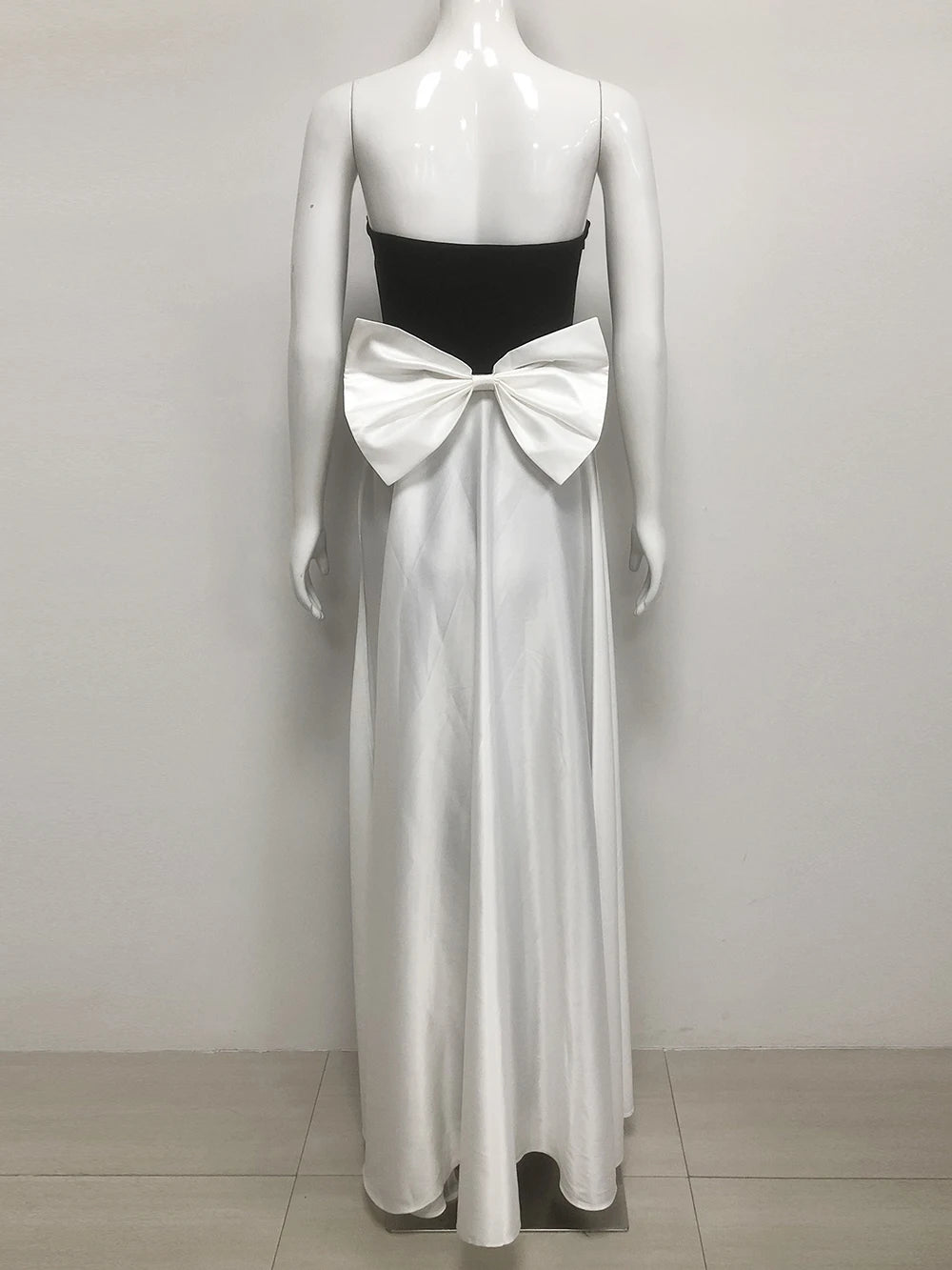 Mannequin wearing a black strapless top and white flowing dress with a large bow on a plain background