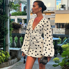 Woman in a polka dot dress standing outdoors with buildings and greenery in the background
