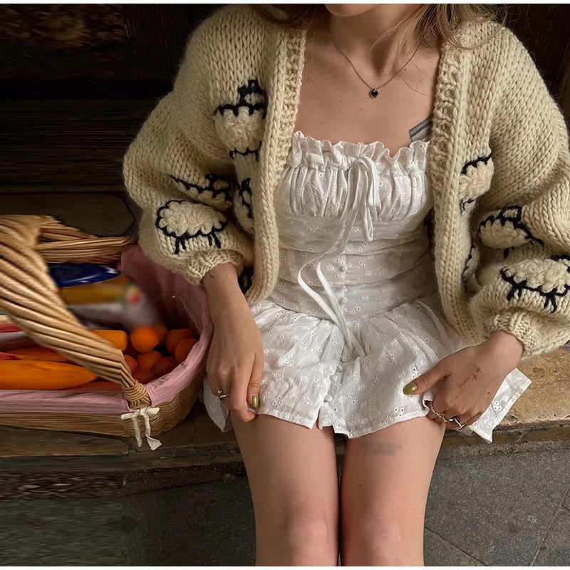 Person wearing a white dress and beige cardigan with cartoon designs, sitting on a bench.