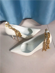 White high-heeled shoes with gold chain details on a light blue background