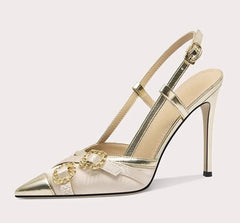 Gold high-heeled shoe with decorative chain on a light gray background
