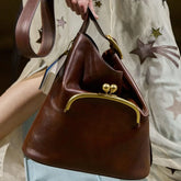 Brown handbag with gold clasp held by a person wearing a star-patterned garment.