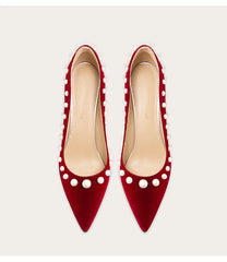 Red high heels with white pearl embellishments on a light gray background