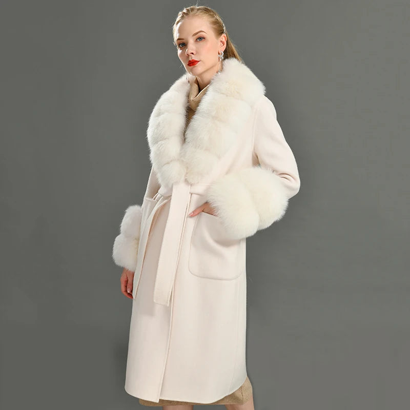 Woman wearing a long cream coat with white fur collar against a gray background