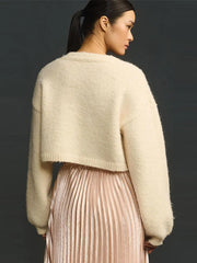 Woman wearing a beige sweater over a pleated skirt against a dark background