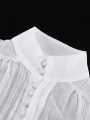 Close-up of a white blouse with fringes and buttons on a black background