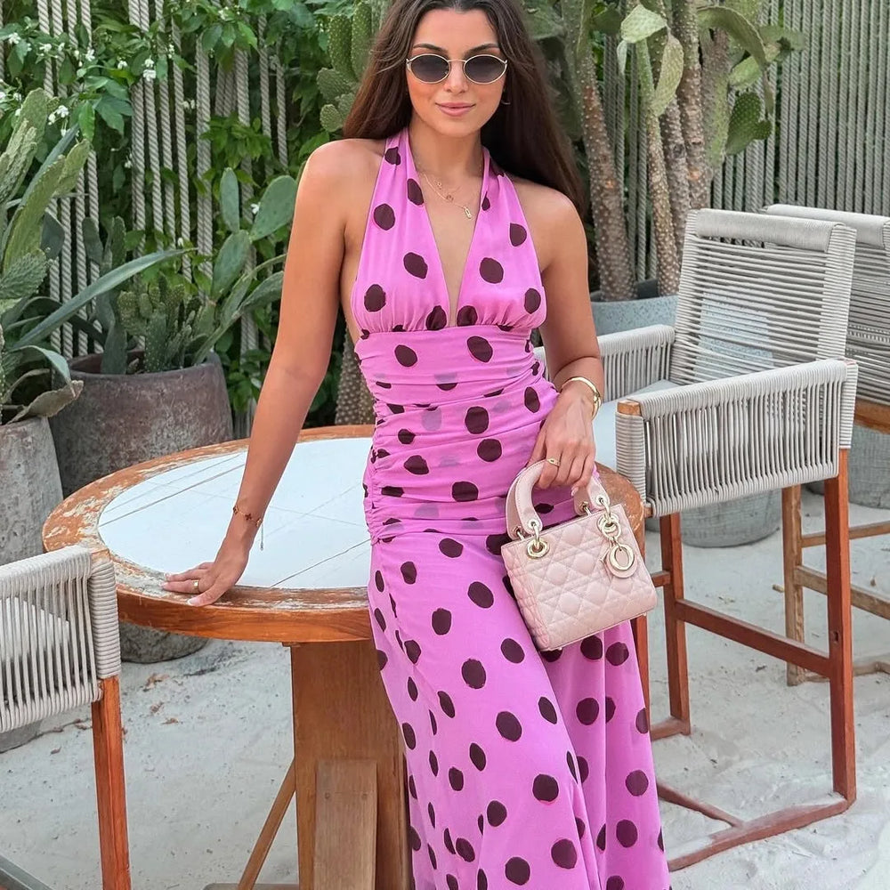Woman in a pink polka dot dress holding a handbag outdoors.
