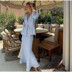 Woman in a light blue outfit standing in an outdoor setting with tables and chairs.