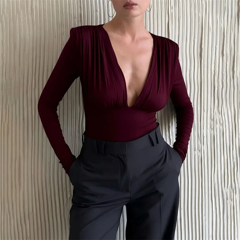 Person wearing a burgundy top and dark pants against a textured wall.