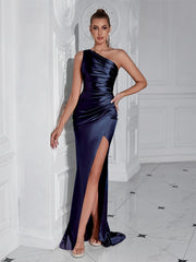 Woman in a one-shoulder navy blue evening gown with a high slit, standing against a white wall.
