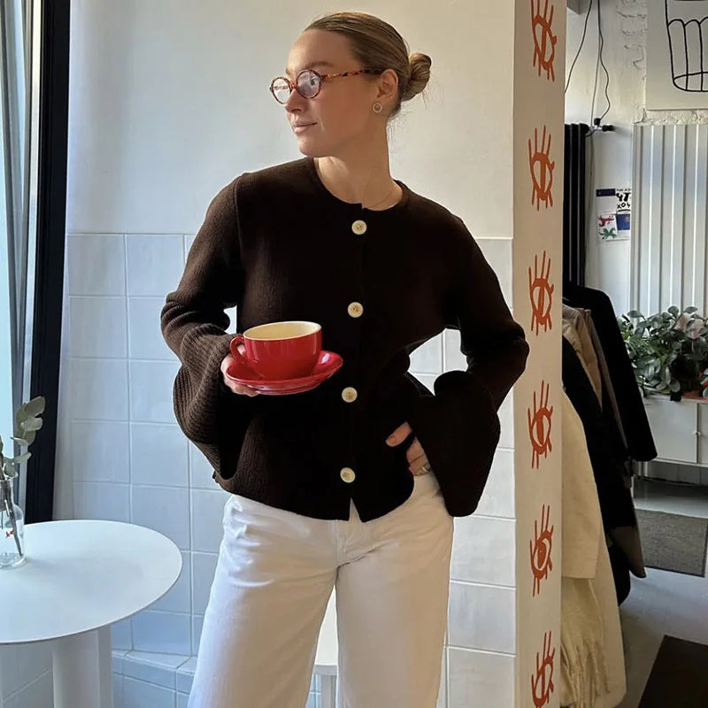 Person holding a red cup and saucer in a room with a white wall and a plant.