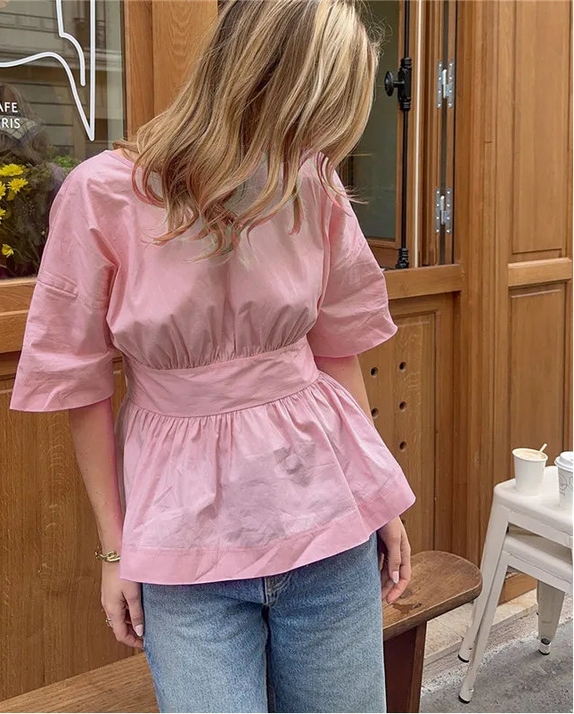 Person wearing a pink top and blue jeans standing in front of a cafe door.