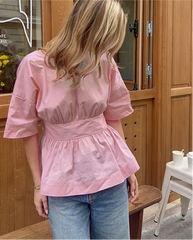 Person wearing a pink top and blue jeans standing in front of a cafe door.