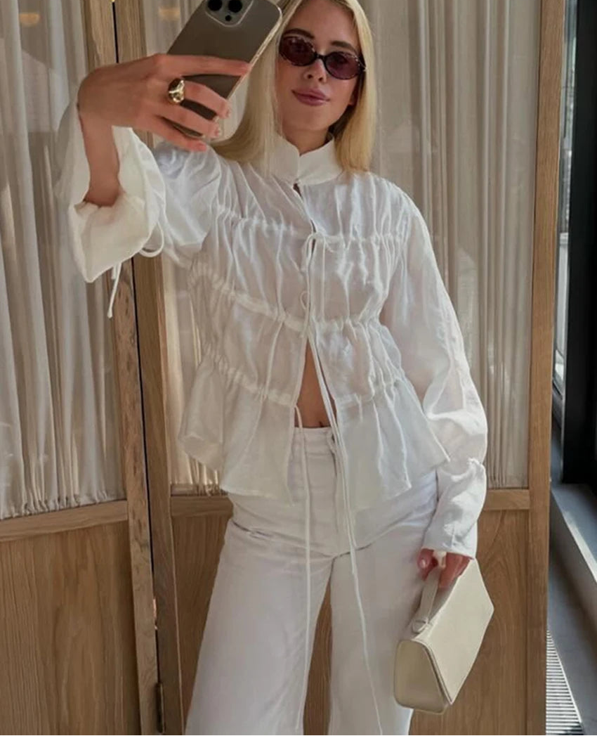 Person taking a mirror selfie wearing a white outfit with a neutral background