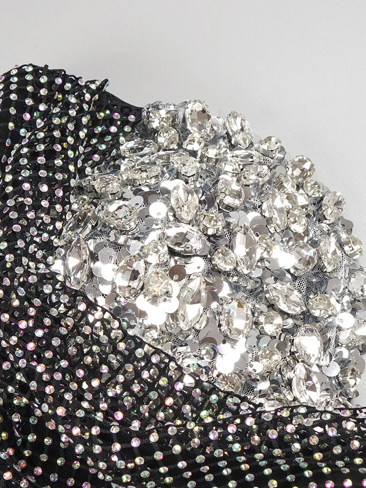 Close-up of a black garment with sparkling silver rhinestone embellishments on a light gray background.