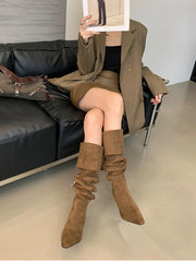 Person wearing brown suede knee-high boots sitting on a black leather couch.