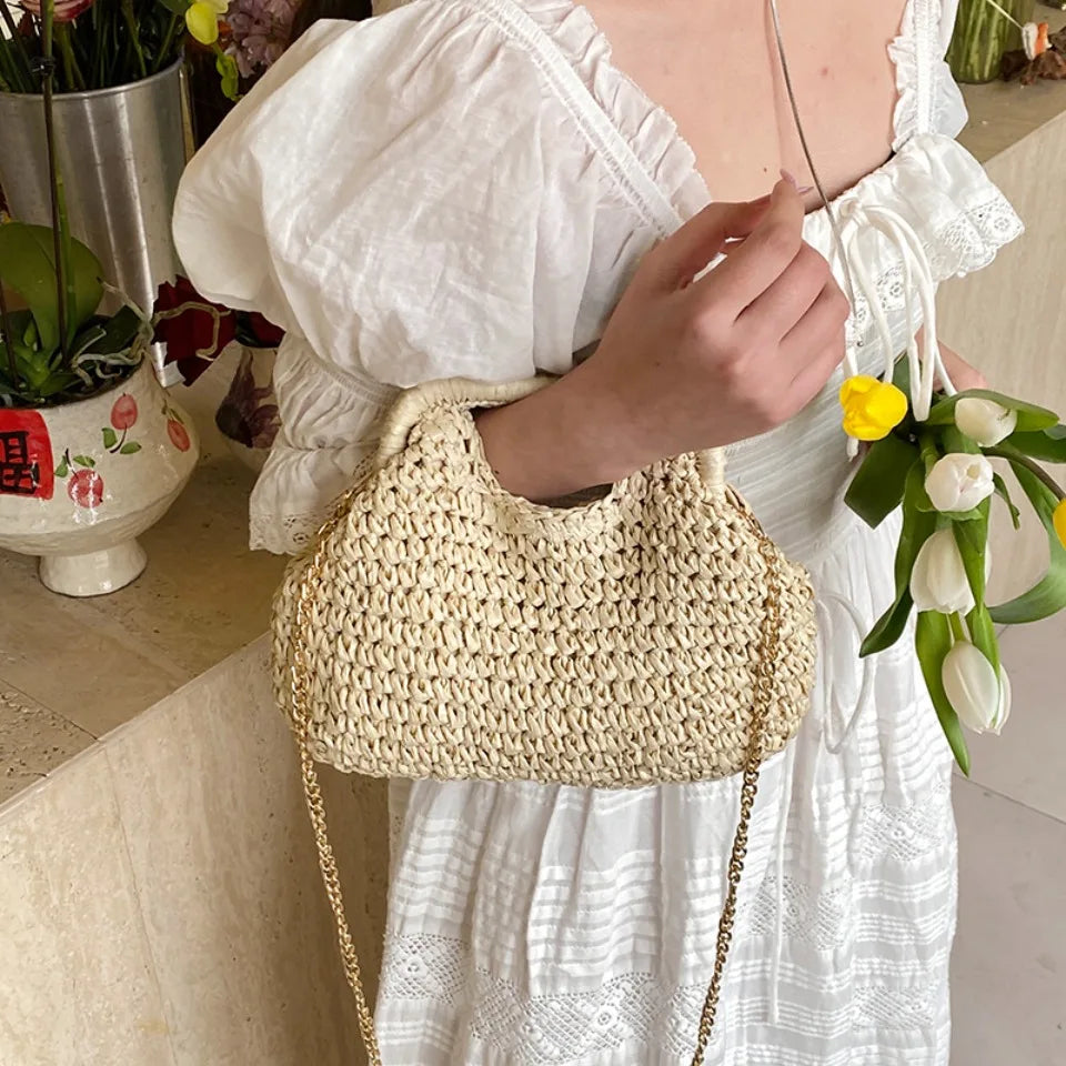 Person holding a woven handbag with a white dress and flowers in a casual setting