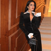 Woman in a black and white outfit holding a black handbag in an indoor setting.