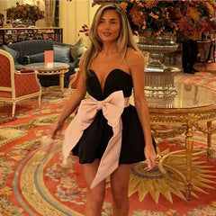 Woman in a black dress with a large pink bow standing in an ornate room.