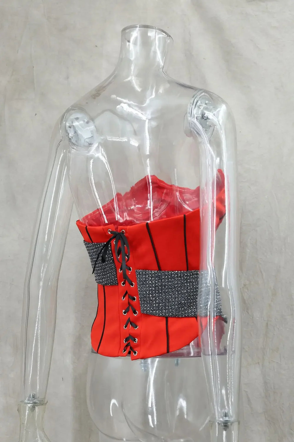 Red corset with black lace-up details on a transparent mannequin against a neutral background