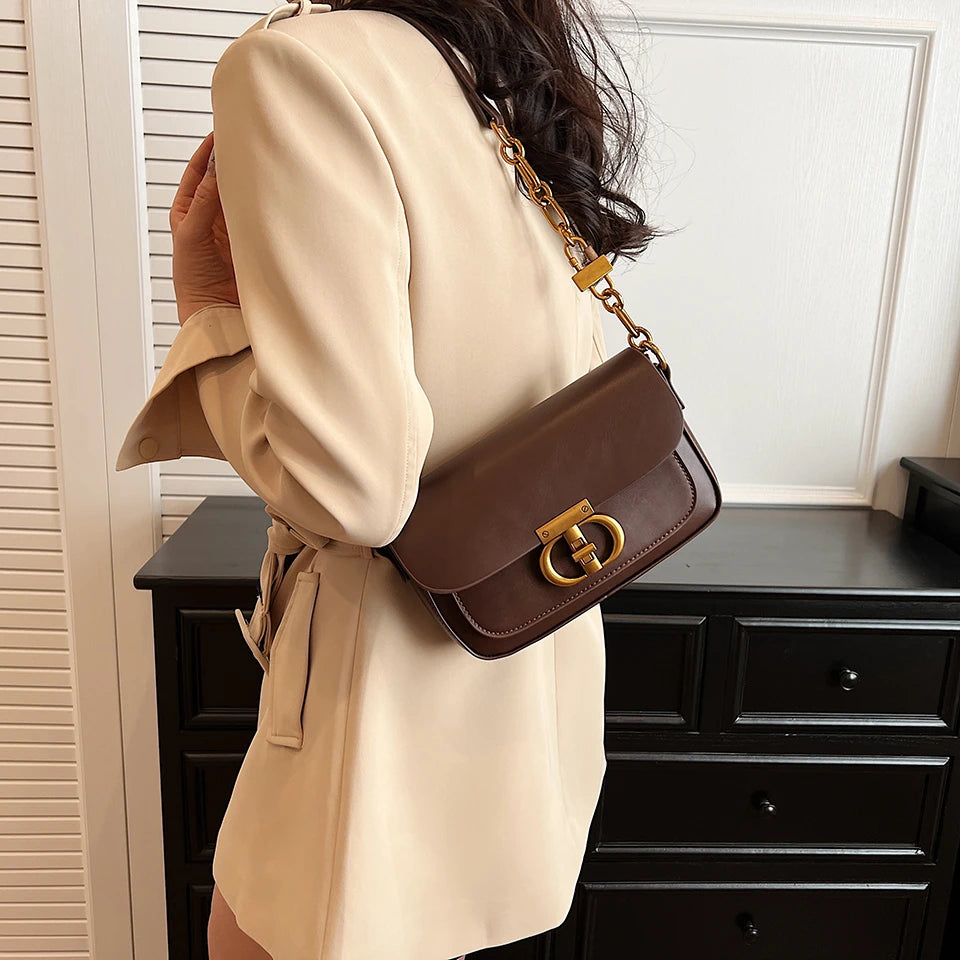 Person wearing a beige coat with a brown handbag featuring a gold clasp.