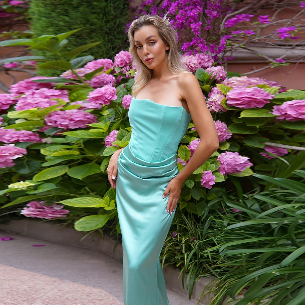 Woman in a teal strapless dress standing in front of pink flowers