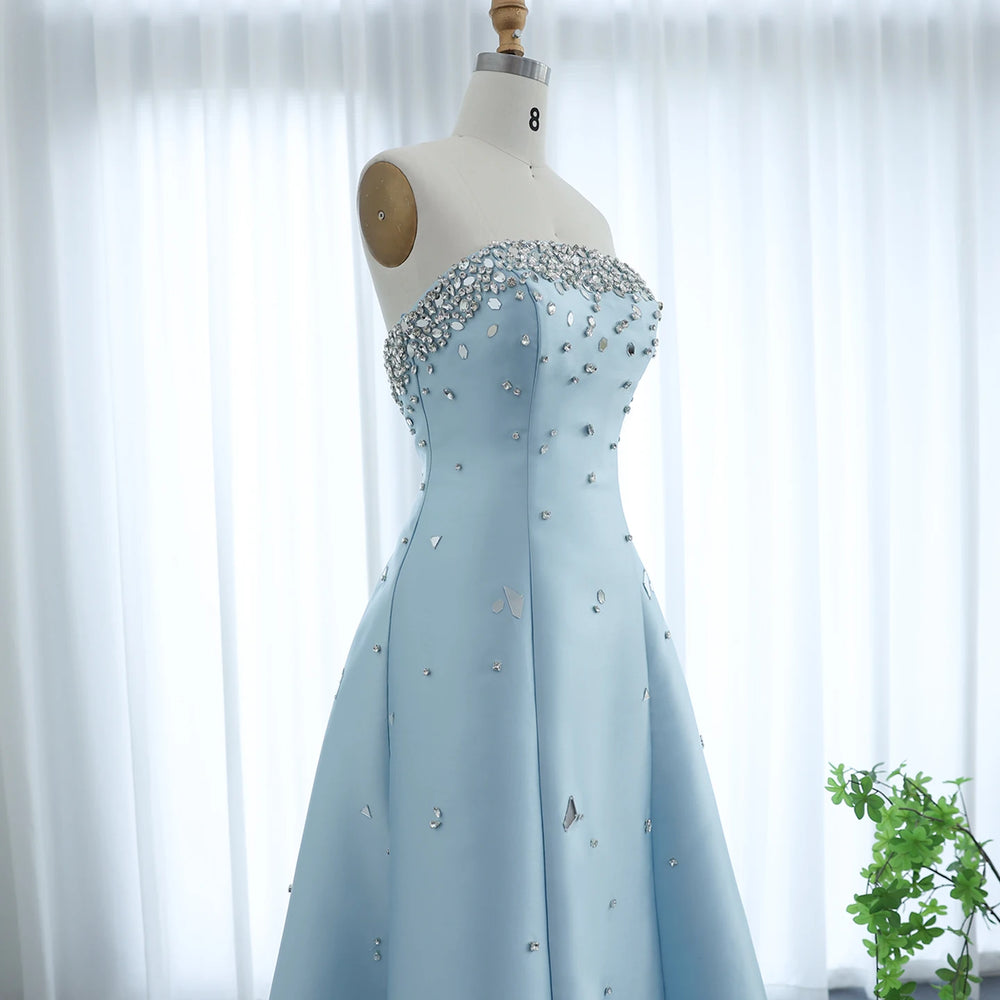 Light blue evening gown with crystal embellishments on a mannequin against a white curtain background.